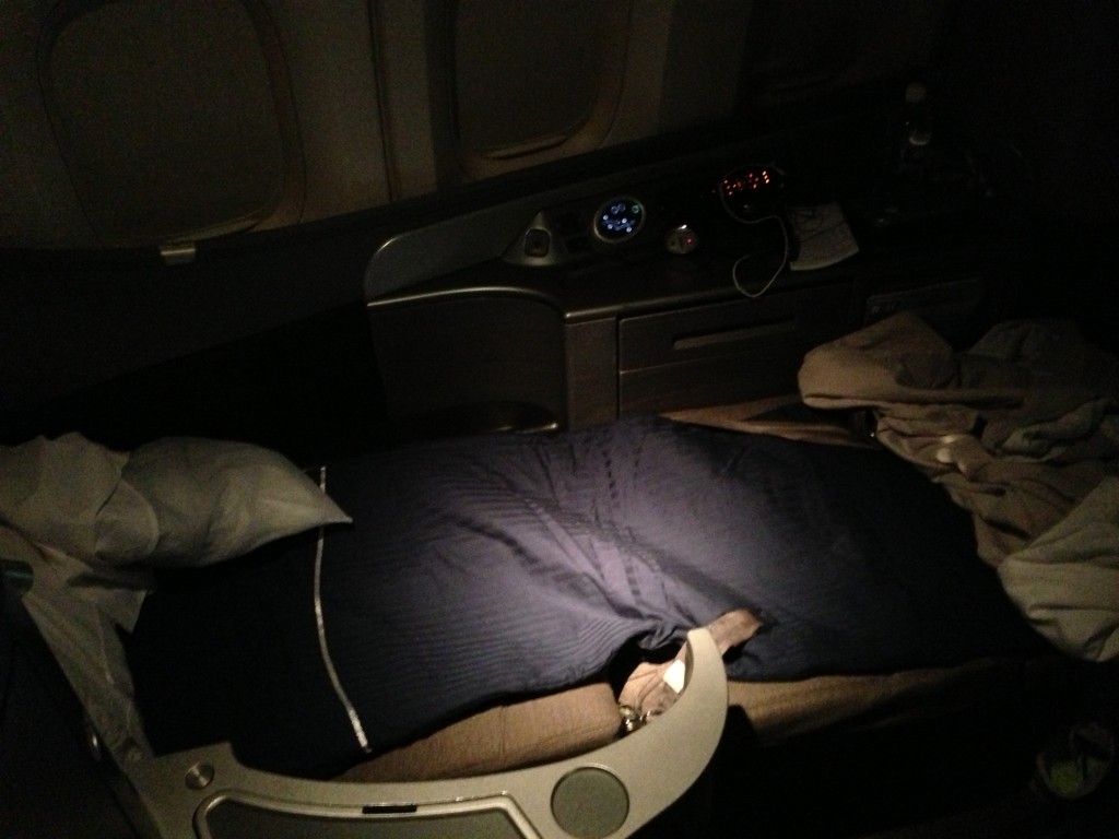 Seat 1A in United Global First Class in bed mode, and made up with a blue duvet